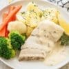 Plate with white fish in creamy sauce, boiled potatoes, lemon, broccoli, carrots, and cauliflower.