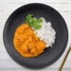 Black plate with white rice, orange curry, cilantro garnish, golden fork, green "GF" label.