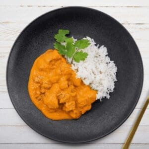 Black plate with white rice, orange curry, cilantro garnish, golden fork, green "GF" label.