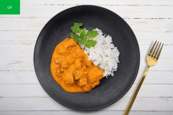 Black plate with white rice, orange curry, cilantro garnish, golden fork, green "GF" label.