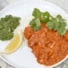 Plate of white rice with red curry, cilantro, green chutney, and a lemon wedge.