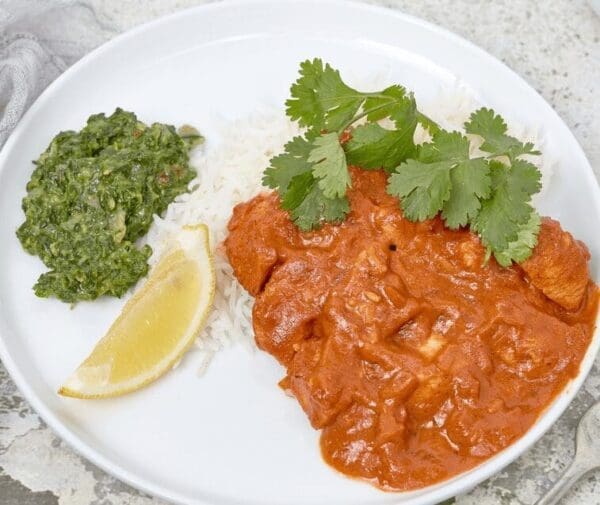 Plate of white rice with red curry, cilantro, green chutney, and a lemon wedge.