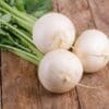 Three white turnips with leafy stems on a rustic wooden surface.