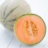 Whole cantaloupe and cut half on light wood, showing orange flesh and seeds.