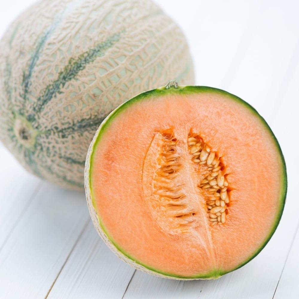 Whole cantaloupe and cut half on light wood, showing orange flesh and seeds.