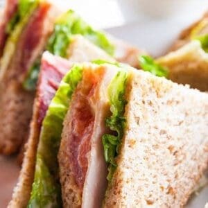 Triangular whole-grain sandwiches with lettuce, tomato, and deli meat on a plate.