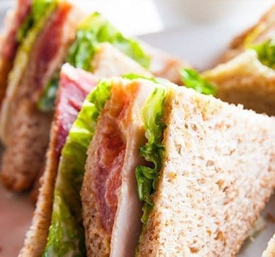 Triangular whole-grain sandwiches with lettuce, tomato, and deli meat on a plate.