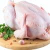 Whole raw chicken on wooden board with garlic, peppercorns, and parsley.