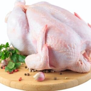 Whole raw chicken on wooden board with garlic, peppercorns, and parsley.
