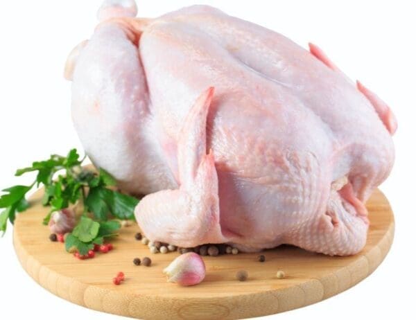 Whole raw chicken on wooden board with garlic, peppercorns, and parsley.