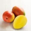 Two whole mangoes and one sliced, revealing bright yellow flesh on light wooden surface.