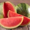 Whole watermelon and slices on wooden surface, green exterior, red interior with seeds.