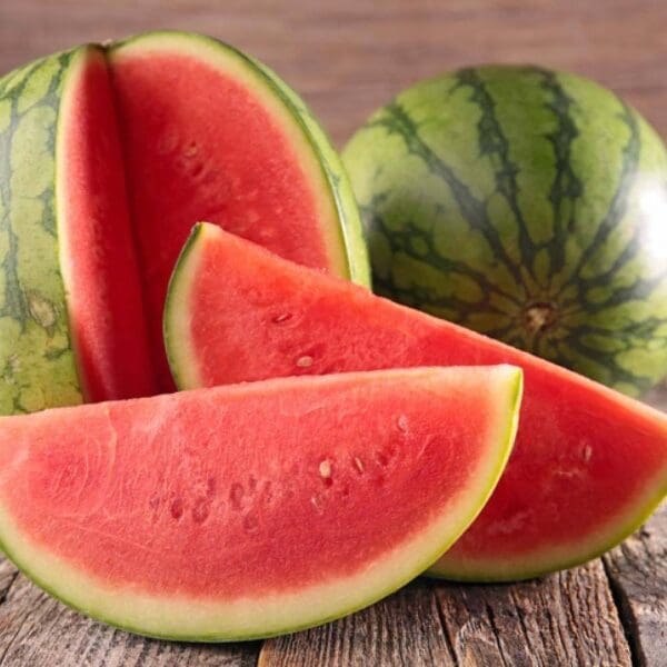 Whole watermelon and slices on wooden surface, green exterior, red interior with seeds.