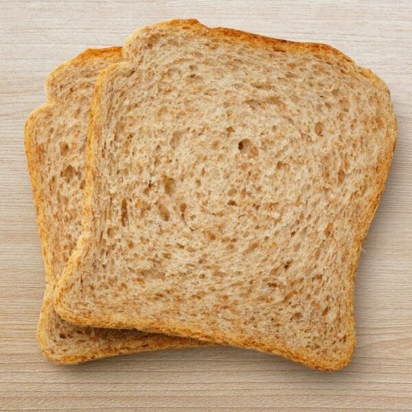 Two whole wheat bread slices on a light wood surface, airy interior, browned crust.