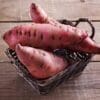 Wicker basket with large reddish-brown sweet potatoes on wooden surface.