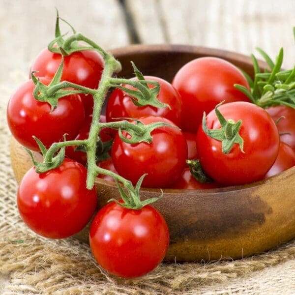 Wooden bowl with red cherry tomatoes on textured fabric surface.