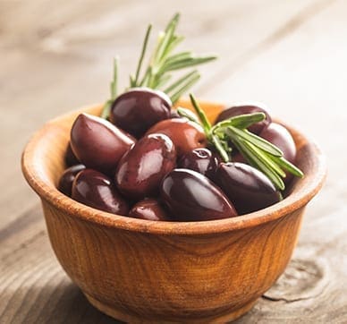 Wooden bowl with dark olives and rosemary on a wooden surface.