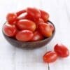 Wooden bowl with small red tomatoes on a light wooden surface.