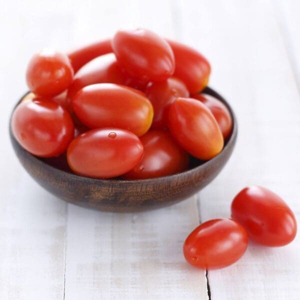 Wooden bowl with small red tomatoes on a light wooden surface.