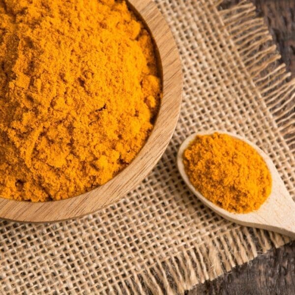 Wooden bowl of yellow-orange turmeric powder on burlap, with matching wooden spoon beside it.