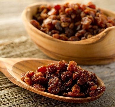 Wooden spoon and bowl with dried raisins on a wooden surface.