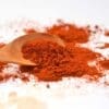Wooden spoon on surface with vibrant red-orange powdered spice spilling out.