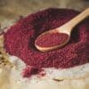 Wooden spoon with red spice on a textured surface.
