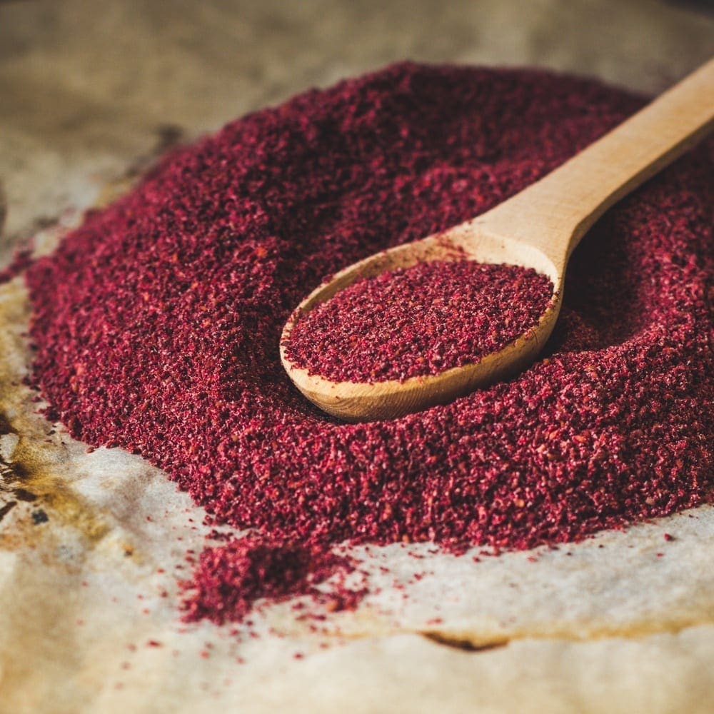 Wooden spoon with red spice on a textured surface.
